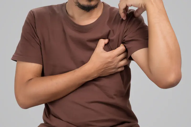 En mann klør seg i armhulen. A man uses his hand to scratch his armpit.
